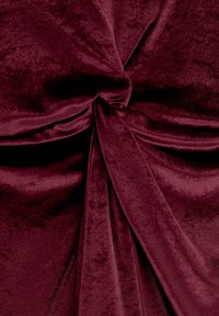 Tissu en velours écrasé rouge bordeaux présentant un détail de nœud torsadé avec des sections drapées, mettant en valeur une texture lisse et une profondeur de couleur riche.