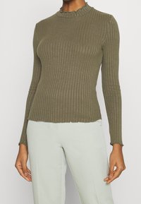 Oliivinvihreä resorinen pitkähiha-paita, jossa on röyhelöity korkea kaulus ja aaltoileva helma. Kangas näyttää pehmeältä ja teksturoidulta.