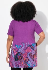 Fialová tunika s krátkými rukávy, s paisley vzorem v modré, růžové a oranžové barvě na lemu. Měkká textura a volný střih.