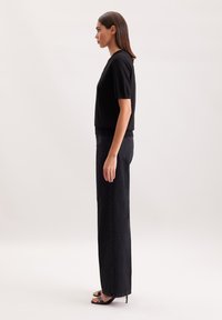 Czarna bluzka z krótkim rękawem zestawiona z czarnymi, wysokopasażowymi spodniami prostymi, o gładkiej teksturze i minimalistycznym wzornictwie. Czarne sandały na obcasie.