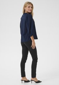 Blusa blu navy in tessuto testurizzato, con maniche a sbuffo e scollatura rotonda. Abbinata a pantaloni neri attillati e mules neri con tacco.