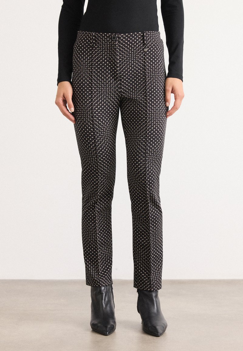 Ces pantalons noirs à motifs présentent une coupe slim, un tissu texturé et un design géométrique distinct avec de petites formes alternées.