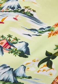 Textil med en ljusgrön bakgrund och ett tropiskt mönster, inklusive berg, palmer och segelbåtar i livfulla färger.