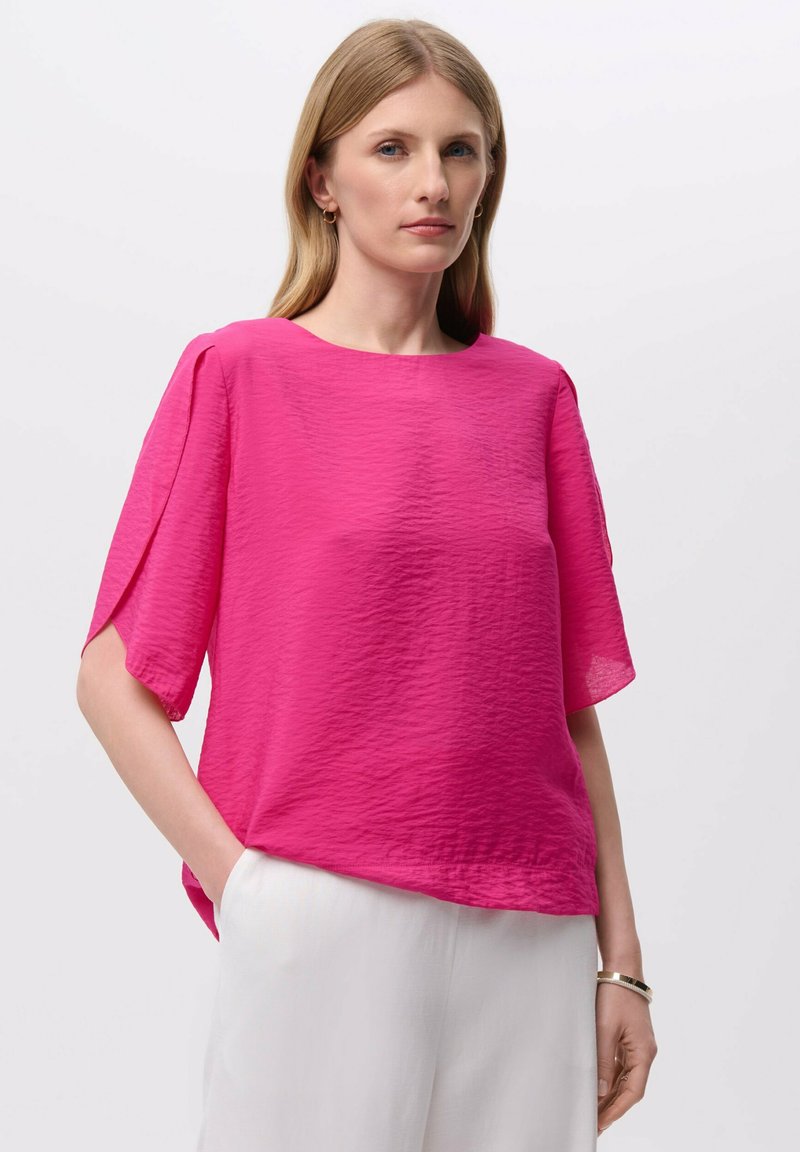 Top fucsia de manga corta con un acabado texturizado y un escote redondeado, combinado con pantalones blancos de corte holgado.