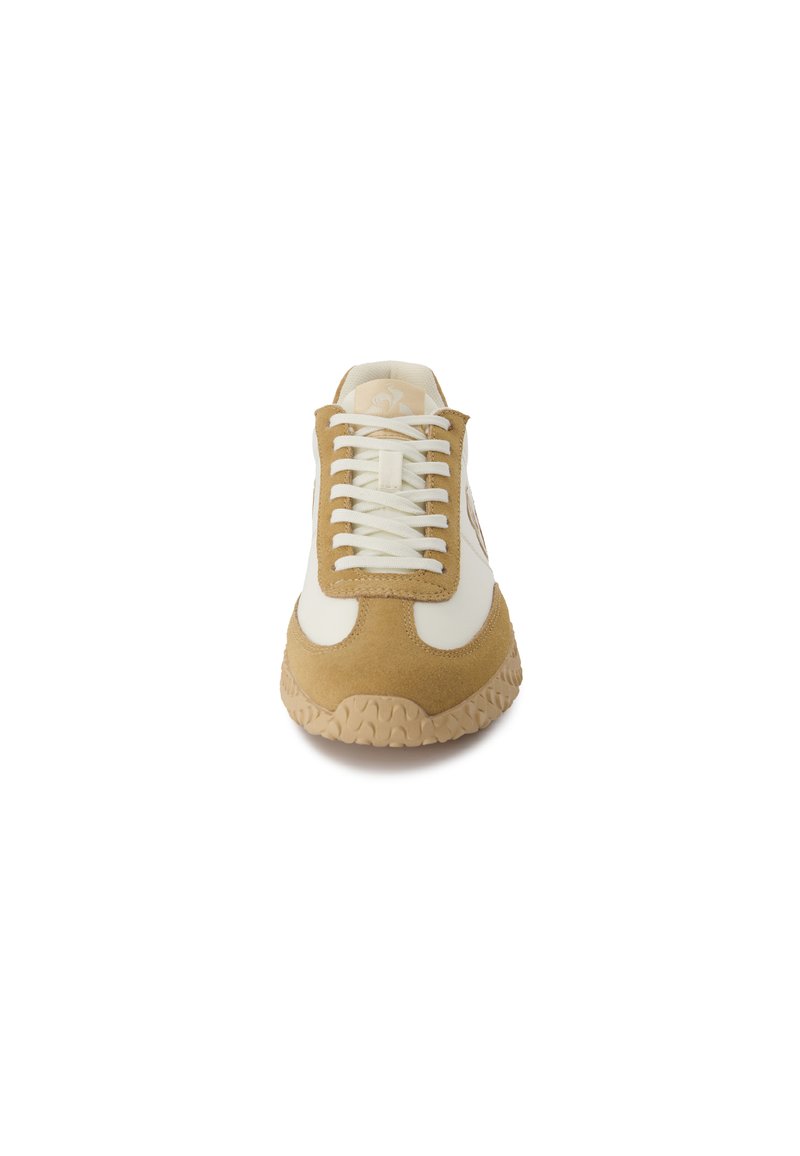 Sneakers beige et crème avec une tige en suède texturé, lacets blancs et une semelle en caoutchouc beige épaisse dotée d'un motif de bande de roulement distinctif.