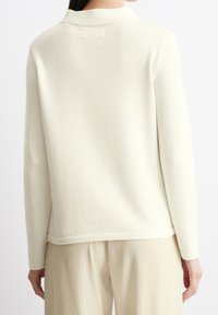Maglione crema, collo a giro, maniche lunghe, texture in maglia morbida, orlo e polsini a costine, design minimale, abbinato a pantaloni beige chiaro.