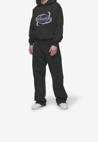 Zwarte hoodie met grafische print en buidelzak, gecombineerd met donker, loszittend broek en witte sneakers. Gestructureerd katoenmateriaal.