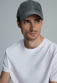 Szara materiałowa czapka z daszkiem z teksturowanym wzorem, w połączeniu z gładką, białą koszulą z okrągłym dekoltem, zdobioną subtelnym haftem.