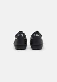 Sapatos Nike pretos com parte superior em couro sintético, aba de calcanhar texturizada e sola de borracha. Apresentam a marca cinza na parte de trás.