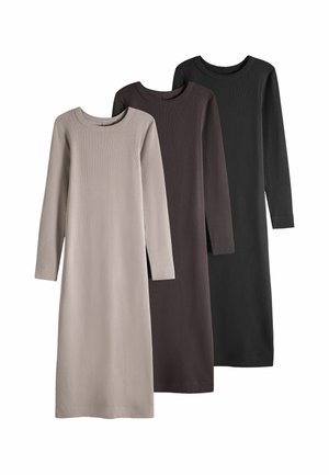 Femme portant une robe longue moulante taupe avec un pull rayé noué autour de la taille et des mocassins marron.