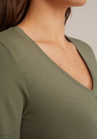 T-shirt vert olive à col en V fabriqué en tissu lisse et extensible, avec des manches courtes et un design ajusté présentant une subtile texture côtelée.