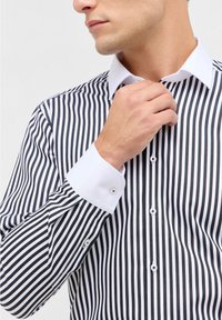 Zwart-wit gestreepte dress shirt met een witte kraag en manchetten, voorzien van knopen langs de sluiting en contrasterende knoopaccenten.