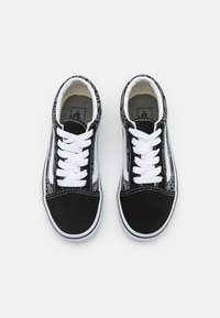 Zapatillas de lona negras con cordones blancos, puntera de ante y paneles laterales con un patrón en blanco y negro. Suelas de goma con bordes blancos.