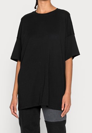 T-shirt nera oversize in cotone, con scollo rotondo e maniche corte, dal taglio morbido e senza motivi o accessori visibili.