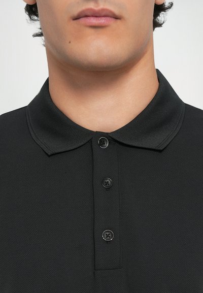 Polo shirt noir avec un tissu texturé, un col classique et trois boutons en noir contrasté. Vue rapprochée.