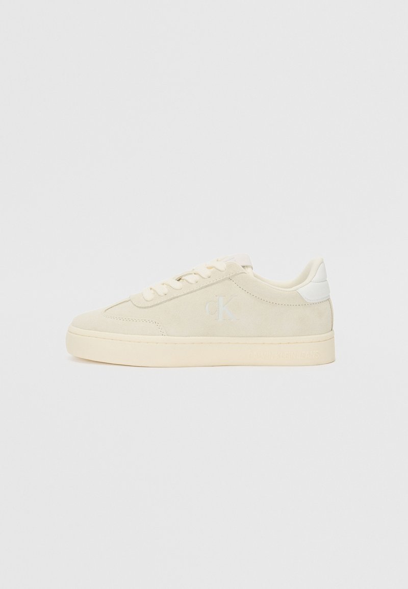 Beige semskinnsneakers med lavt design, snøring og lyse detaljer. Preget logo og teksturert mellomsåle.