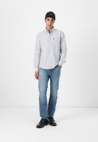 Stripet skjorte med knapper i hvit og blå, med en rød logo på brystet; kombinert med lyseblå jeans og svarte sko. Caps inkludert.