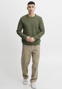 Groene gestructureerde trui met een ruitpatroon, ronde halslijn, gecombineerd met beige broek en witte sneakers. Eenvoudige, casual look.