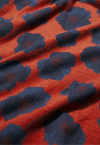 Puha szövet nagy sötétkék virágmintával, textúrált narancssárga háttéren, enyhén gyűrött.