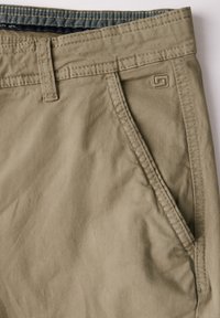 Khaki shorts made of soft fabric, featuring a flat front, side pockets, and a subtle logo detail near the waistband. Smooth texture.