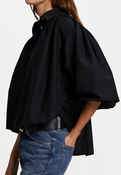 Svart oversized skjorte i lett bomull. Har krage, knappeåpning og vide ermer. Kombinert med blå denim jeans.