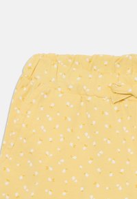 Gule bomullsshorts med en teksturert midje, knytedetalj og et hvitt blomstermønster med små gule accenter.