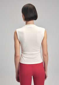 Vit utan ärmar topp med en figurnära design och rynkad ryggdetalj, kombinerad med högmidjade röda leggings. Slätt, stretchigt tyg.