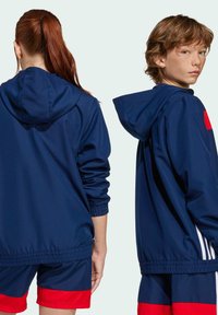 Veste à capuche bleu marine avec des poignets et un ourlet élastiques, dotée d'un accent rouge sur la poitrine, associée à un short de sport bleu marine et rouge.