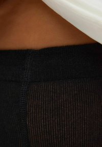 Svarta stickade leggings med en texturerad yta, med en bred midjeresår och en halvgenomskinlig nedre del.