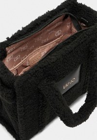 Borsa in pelliccia sintetica nera con manici corti, chiusura con zip e un interno rosa chiaro a contrasto con motivo logo. Include una tasca interna.