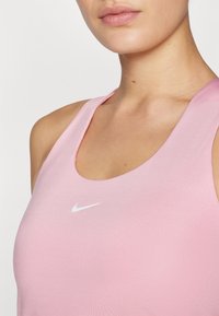 Pink atletisk tanktop med rund halsudskæring og tynde stropper, med en lille hvid Nike-logo på forsiden, lavet af glat, elastisk materiale.