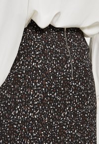 Svart tygkjol med ett spritt mönster av vita och rostfärgade prickar, med en synlig siddragkedja och en mjuk yta.