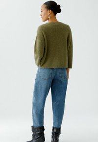 Green, fluffy knit sweater with a relaxed fit and long sleeves, paired with light blue, loose-fitting jeans and black, folded ankle boots.
