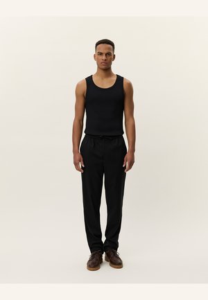 Black sleeveless tank top pairs with black trousers and brown shoes. The outfit features a simple design with a smooth texture.