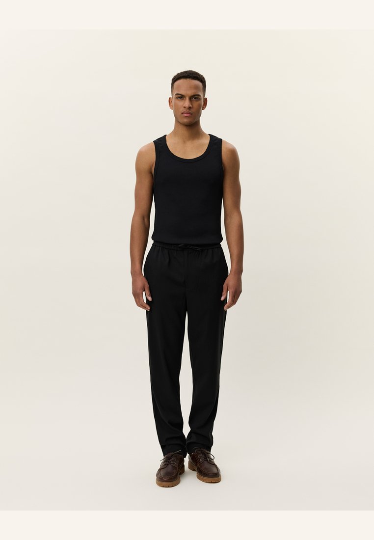 Zwarte mouwloze tanktop gecombineerd met zwarte broek en bruine schoenen. De outfit heeft een eenvoudig ontwerp met een gladde textuur.