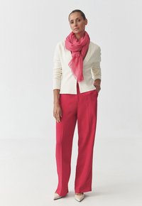 Cardigan crema, sciarpa rosa e pantaloni larghi rossi. La sciarpa ha una texture morbida; l'insieme presenta un design sartoriale e décolleté neutri.