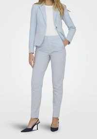 Ljusblå randig kostym med en åtsittande kavaj och skräddarsydda byxor. Slät tyg med lätt glans, kombinerad med marinblå slingbacks.