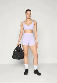 Gaiši violeta sporta krūšturis un šorti, izgatavoti no elastīga auduma. Melns sporta somas roka, melnas sporta apavu un baltas īsās zeķes.