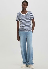 Gestreiftes navyblaues und weißes T-Shirt mit kurzen Ärmeln, kombiniert mit hellblauen Weitbeinform-Jeans und weißen Sneakern, mit einem runden Ausschnitt und dezentem Branding.