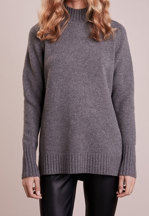 Grau gestrickter Pullover mit Rundhalsausschnitt, gerippten Bündchen und Saum, mit weicher Textur und lässiger Passform. Kombiniert mit schwarzen Lederhosen.