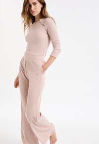 Set di loungewear a costine rosa chiaro composto da una maglia aderente con maniche lunghe e un dettaglio discreto sulla spalla, e pantaloni a vita alta a gamba larga.