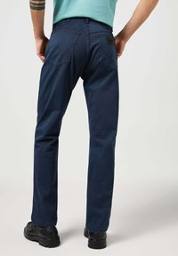 Pantalones azul marino hechos de una mezcla de algodón con corte recto. Cuenta con dos bolsillos traseros y sutiles detalles de costura.