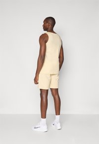 Beige bomullstopp och shorts, figurnära design, slät textur. Bärs med vita sneakers och strumpor i ankellängd. Enkel och minimalistisk look.