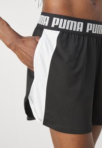 Mustat urheilushortsit, joissa on valkoinen sivupaneeli, joustava vyötärö, jossa on "PUMA"-teksti, tekstuurinen kangas ja sivutasku.