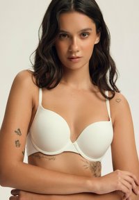 Biały miękki stanik z regulowanymi ramiączkami, gładk�ą teksturą i dekoltem w kształcie litery U. Posiada zapięcie z przodu i minimalistyczny design.