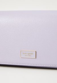 Lilac leather wallet with a textured finish, featuring a gold-tone logo plate and contrasting stitching along the edges.