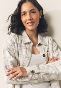 Světle krémová bavlněná bunda s modro-hnědým kostkovaným vzorem, zapínáním na knoflíky vpředu a texturovanou látkou.