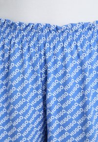 Blå shorts med ett heltäckande, upprepat mönster av den vita "HUGO"-logotypen. Den elastiska midjebanden möjliggör justerbar passform; slät tygtextur.