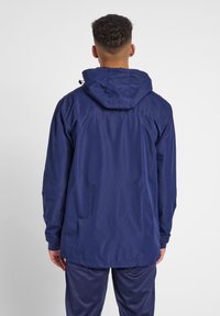 Giacca leggera blu navy con cappuccio, dalla texture liscia, con una vestibilità comoda e polsini elastici, cuciture visibili sulle spalle e sulla schiena.