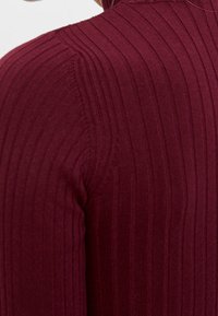 Bourgogne-randig tröja med långa ärmar, som har vertikala linjer och en texturerad tyg. Halslinningen har en enkel, rund form.